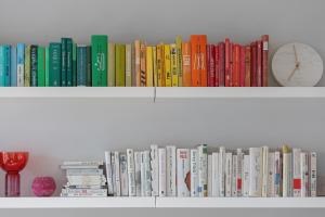 a row of books on a shelf with a clock at Cozy Apartment Gieysztora Wilanów by Renters in Warsaw