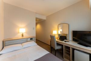 a hotel room with a bed and a desk with a television at HOTEL MYSTAYS Kanazawa Katamachi in Kanazawa