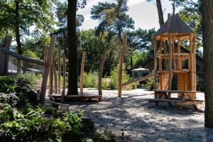 un parque infantil con columpios de madera y un árbol en Vakantiepark Latour, en Oirschot