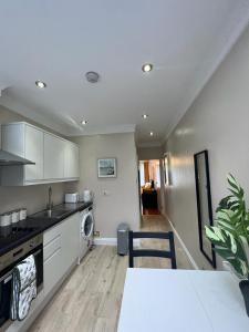 une cuisine avec des armoires blanches, une table et une cuisinière dans l'établissement JAN'S HAVEN Wembley Park - lovely 1 bedroom flat, sleeps 4, free parking, 10 minutes from Wembley stadium and Wembley Park station, à Londres