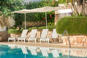 un grupo de sillas y una sombrilla junto a la piscina en Hotel Cala Dor - Adults Only, en Cala d´Or