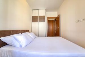 uma cama com lençóis brancos e almofadas num quarto em Gold apartman em Podgorica