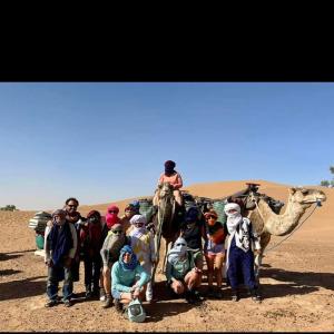 a group of people standing in the desert with camels at Mhamid wild Trekking Camels in Mhamid