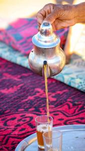 a person pouring a tea pot into a glass at Mhamid wild Trekking Camels in Mhamid