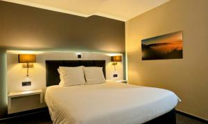 a bedroom with a large white bed with two lamps at Hôtel L'Amandier in Libramont