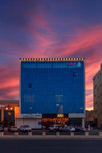 Arica hotel apartments في تبوك: مبنى ازرق كبير فيه سيارات تقف امامه