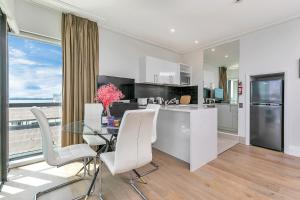 a kitchen with a glass table and white chairs at Exquisite Sun Soaked Corner Apartment in Auckland