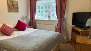 1 dormitorio con 1 cama con almohadas rojas y TV en The Cricketers Inn, en Winchester