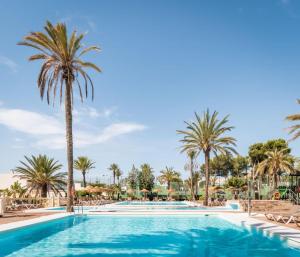 a swimming pool with palm trees and chairs at Hotel Portomagno by ALEGRIA in Aguadulce