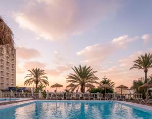 una piscina en un complejo con palmeras y sombrillas en Hotel Portomagno by ALEGRIA, en Aguadulce