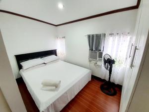 a bedroom with a white bed and a fan at Calapan Transient House Acacia L35 in Calapan