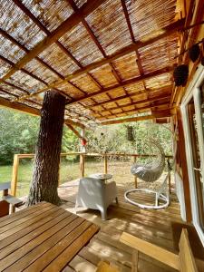 une terrasse en bois avec un arbre et un plafond en bois dans l'établissement Cabane de charme en pleine forêt - Domaine Temali, à Labouheyre