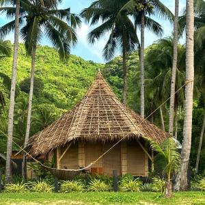 a straw hut with a hammock in front of palm trees at Eco Sanctuaries Nature Lodge Nacpan Beach, El Nido in El Nido