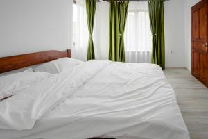 a white bed in a bedroom with green curtains at Cabana FloriDeea in Scrind-Frăsinet