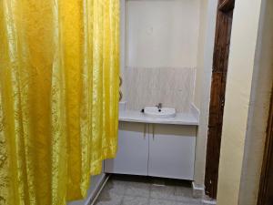 La salle de bains est pourvue d'un rideau de douche jaune et d'un lavabo. dans l'établissement Airport Studio Apartments-JKIA, à Nairobi