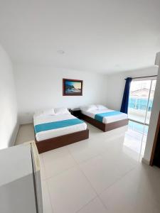 two beds in a white room with a window at Hotel AguaMarina Rodadero Santa Marta in Gaira