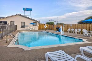 einen Pool mit weißen Stühlen und einem Zaun in der Unterkunft Motel 6-Bryan, TX - College Station in Bryan