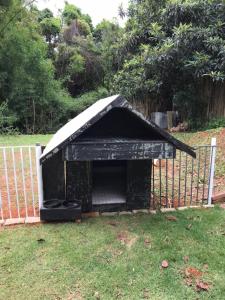 a black doghouse in the grass next to a fence at Casa aconchegante in Bragança Paulista