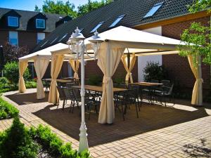 un patio con mesas y sillas bajo una sombrilla blanca en Hotel Flora, en Fredersdorf