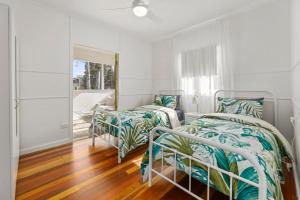 two beds in a white room with wood floors at Entire Beach House on Bribie Island in Bongaree