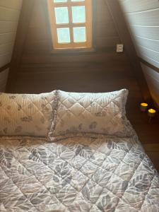 a bed with a pillow and a window in a attic at Glamping casal - mini chale mobiliado com colchão casal roupa de cama travesseiros - Rancho Perene estação rural in Jaraguá do Sul