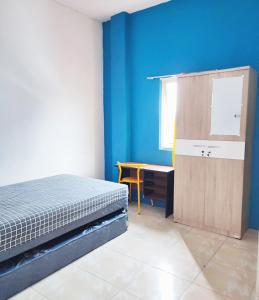 um quarto com uma cama, uma secretária e paredes azuis em Kost Griya Hikari by Ecommerceloka em Jakarta