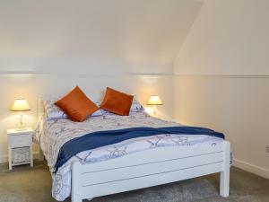 a white bed with two orange pillows on it at Anchor Cottage in Portpatrick