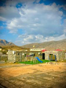 a playground in front of a building with mountains in the background at Jabal Shams Al-Salam house in Sa‘ab Banī Khamīs