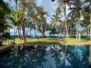 a pool with palm trees and the ocean in the background at Amatapura Beachfront Villa 10 , SHA Certified in Ao Nam Mao