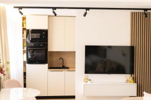 a kitchen with white cabinets and a large tv on the wall at Soho Boutique Apartman in Požega