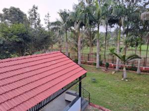 a building with a red roof and some palm trees at Kolluri Nest Farm villa airport mysuru in Kadakola