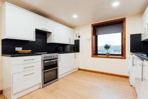a kitchen with white cabinets and a window at The Barn @ Clauchan holiday Cottages in Gatehouse of Fleet +9 photos