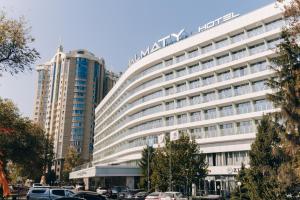 a large white building with cars parked in front of it at Almaty Hotel in Almaty