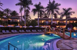 un puente sobre una piscina en un complejo con palmeras en Seaside Grand Hotel Residencia - Gran Lujo, en Maspalomas