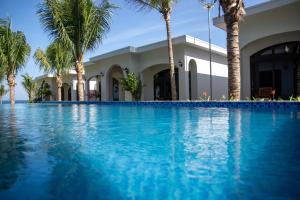 a swimming pool in front of a house with palm trees at La'mer Villa Mũi Né in Phan Thiet