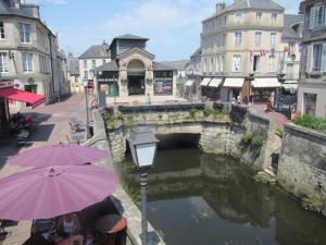 un puente sobre un río en una ciudad con gente sentada bajo sombrillas en La Plus Petite Maison De France, en Bayeux