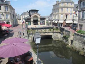 a bridge over a river in a city with people sitting under umbrellas at La Plus Petite Maison De France in Bayeux
