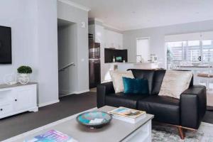 a living room with a black couch and a kitchen at Beachside Townhouse in Mornington