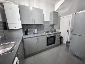 a kitchen with white cabinets and a sink and a refrigerator at Modernised 3 Bedroom House, Lascelle Residence in Roundhay