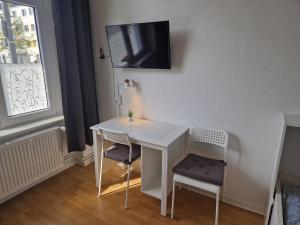 een witte tafel met twee stoelen en een tv aan de muur bij Zimmervermietung Berlin Mertens in Berlijn