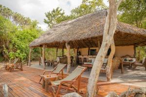 a large wooden deck with chairs and a thatch roof at Selous River Camp in Kwangwazi
