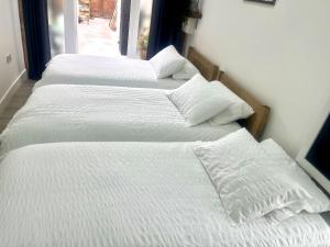 a group of three white beds in a room at Nice and Cosy Large Studio near Luton Airport in Luton