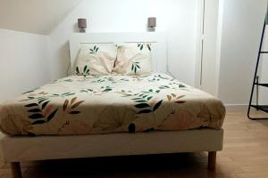 ein Bett mit einer weißen Tagesdecke mit Blättern darauf in der Unterkunft La Tranquillité in Laroche-Saint-Cydroine