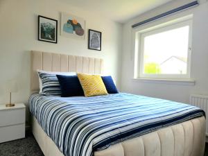 a bedroom with a bed with a striped comforter and a window at Tranquil Home Away from Home in Newton Mearns
