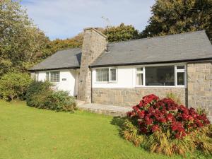 a white house with red flowers in the yard at Ty Cerrig in Pwllheli