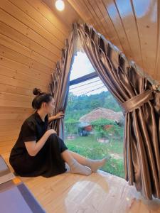 Una mujer sentada en una habitación mirando por la ventana en Xuhao Homestay en Hanoi