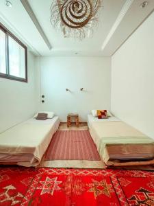 2 camas en una habitación blanca con alfombra roja en DesArt Appartment, en Tamraght Ouzdar