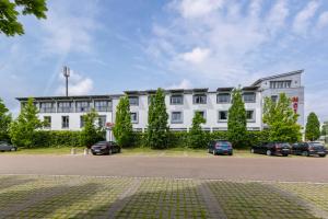 un grand bâtiment blanc avec des voitures garées devant lui dans l'établissement Hotel Leipheim Süd, à Leipheim