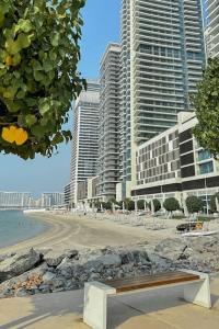 a bench sitting on a beach with tall buildings at Clever Guest Beach Vista 1 in Dubai