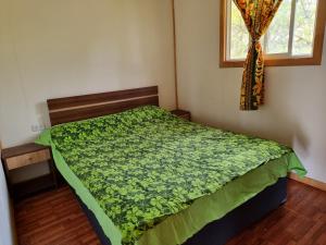 ein Schlafzimmer mit einem Bett mit einer grünen Bettdecke und einem Fenster in der Unterkunft Mika's House 2 in Hanga Roa